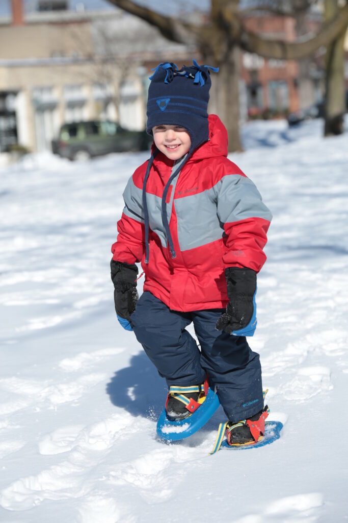 Snow day in Petoskey. A child walks with snow shoes through the park.